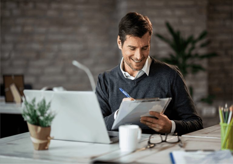 business man signing document, sat at desk and laptop